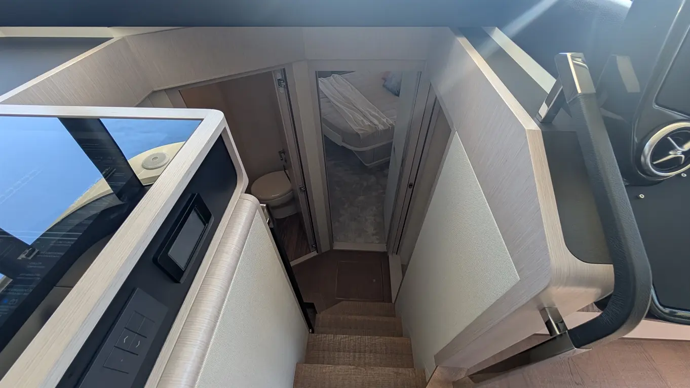 Modern boat interior view, showing stairs leading to a cabin with a bed, a bathroom door, and sleek cabinetry.